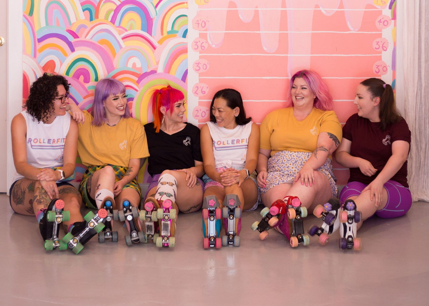 Six roller skaters in roller skates and rollerfit merchandise sitting down having a conversation.