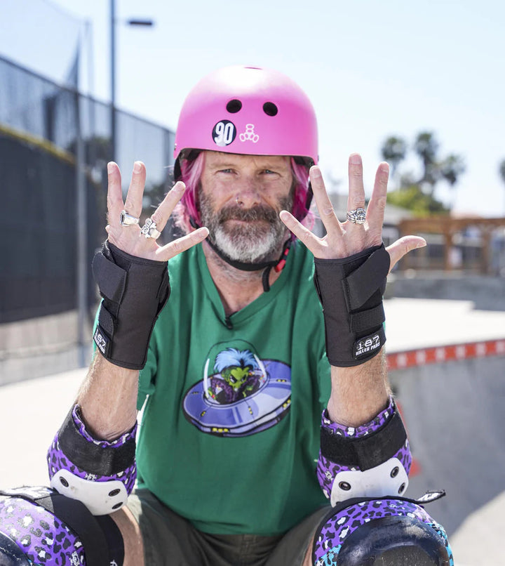 Person wearing a pink helmet and protective gear, showing off 187 Killer Pads Pro Wrist Guards