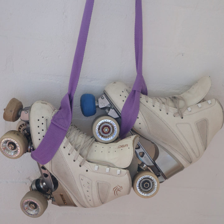 White artistic roller skates hanging using the Violet RollerFit Roller Skate Leash