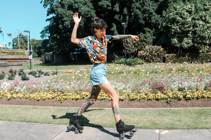Ash is wearing a bright short, denim shorts and Ash with tattooed legs wears Chuffed Skates Wanderer roller skates in Vegan Black whilst doing a heel-toe manual.