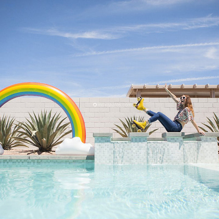Stacey sits poolside wearing Pineapple yellow Lolly roller skates, jeans and a bright pattern t-shirt.
