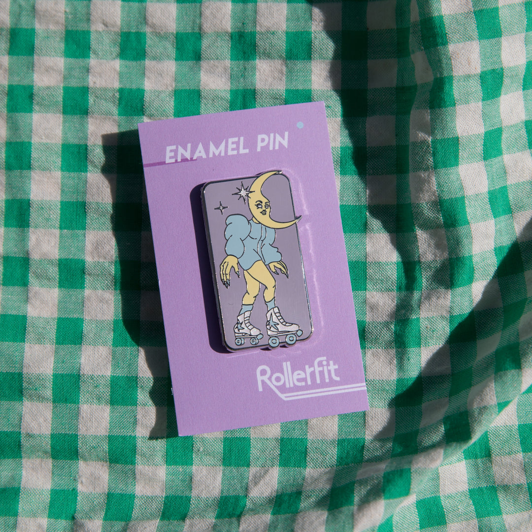 RollerFit Celestial Skater enamel pin with pastel lavender background, blue and yellow character and white glitter stars and roller skates.
