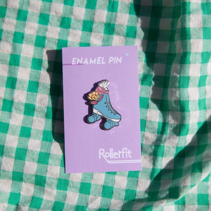 RollerFit Galah enamel pin with blue and white roller skate, pastel yellow flower and sparkly pink galah head.