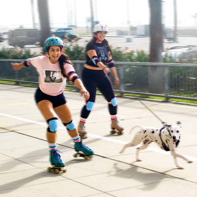 Legs and Michelle skating fast along a boardwalk with a dalmatian dog on a lead white wearing Triple 8 sunset covert pads.