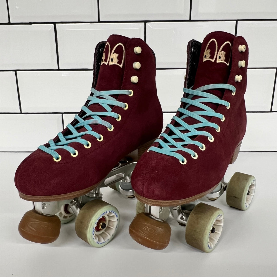 Pair of burgundy Chuffed custom setup roller skates with light blue laces on a white tiled background