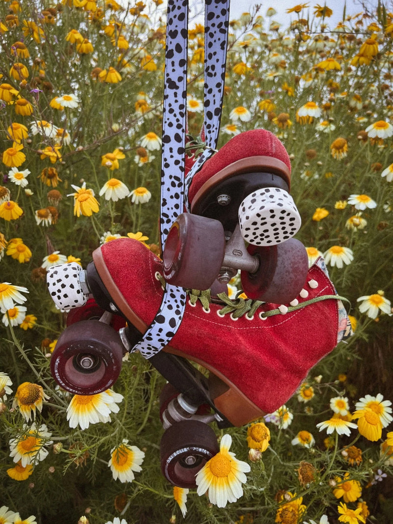 Red roller skates held by Muse Skate Co. Dalmatian spot skate leash in a daisy field.