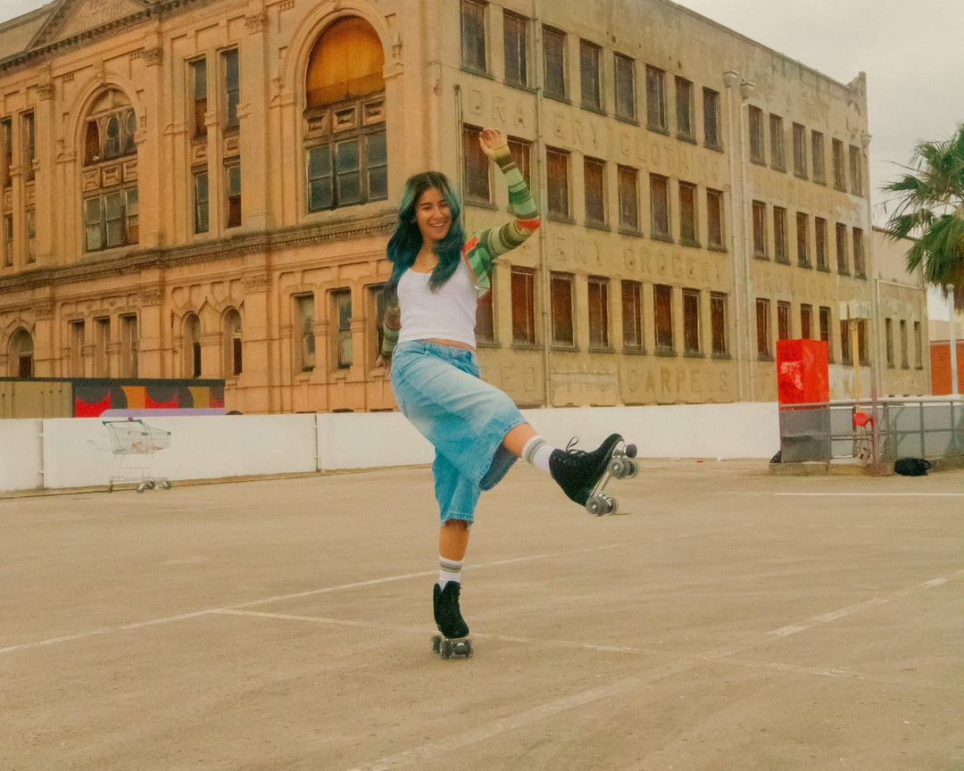 Rib skates in a carpark wearing a white and green top, light denim jorts, white socks and Chuffed Skates Wanderer Roller Skates in Black - a sleek looking suede skate.