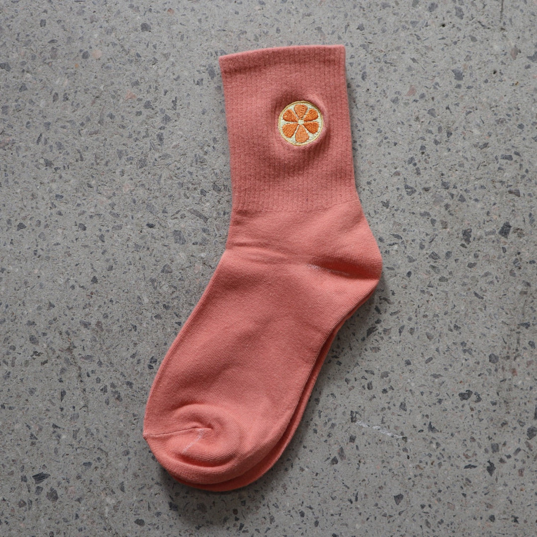 Orange RollerFit sock with orange slice embroidered design on a gray surface