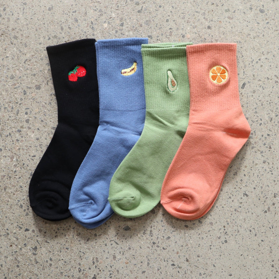 Four colorful RollerFit socks with fruit designs on a concrete surface
