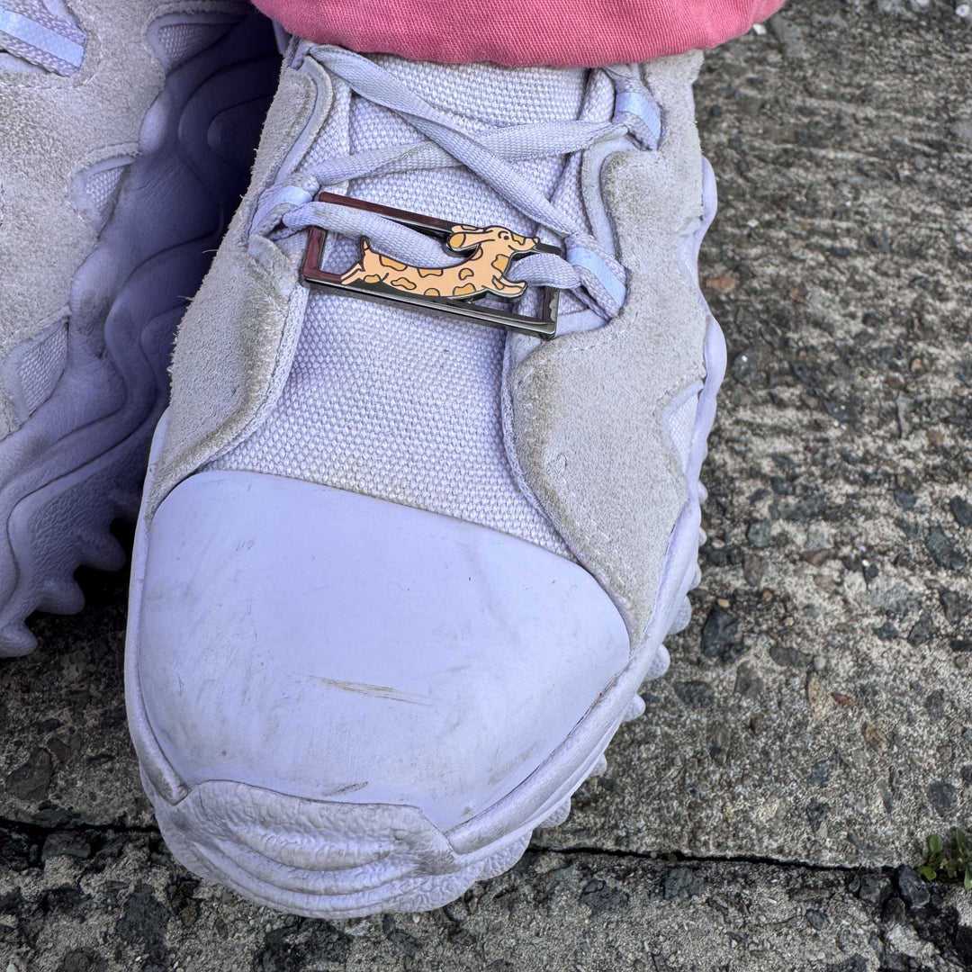 Lilac sneaker with a RollerFit Daphne Sausage (cartoon sausage dog) lace lock threaded through the laces.
