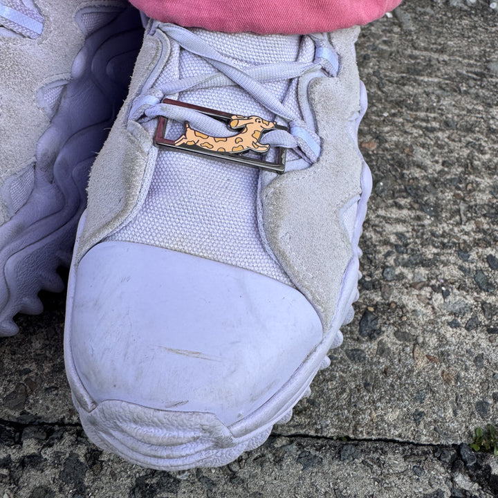 Lilac sneaker with a RollerFit Daphne Sausage (cartoon sausage dog) lace lock threaded through the laces.
