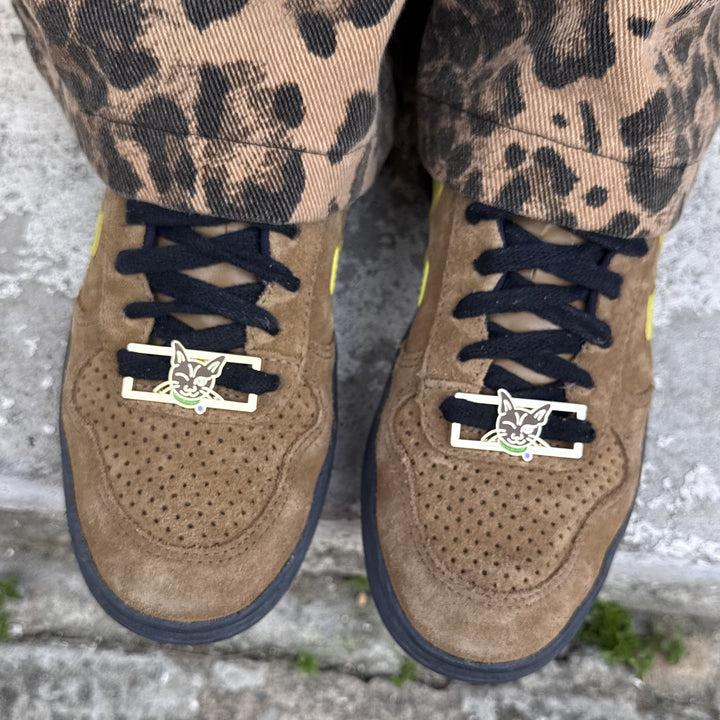 Brown suede shoes with RollerFit Whiskey Bones cat face lace locks on a concrete surface.
