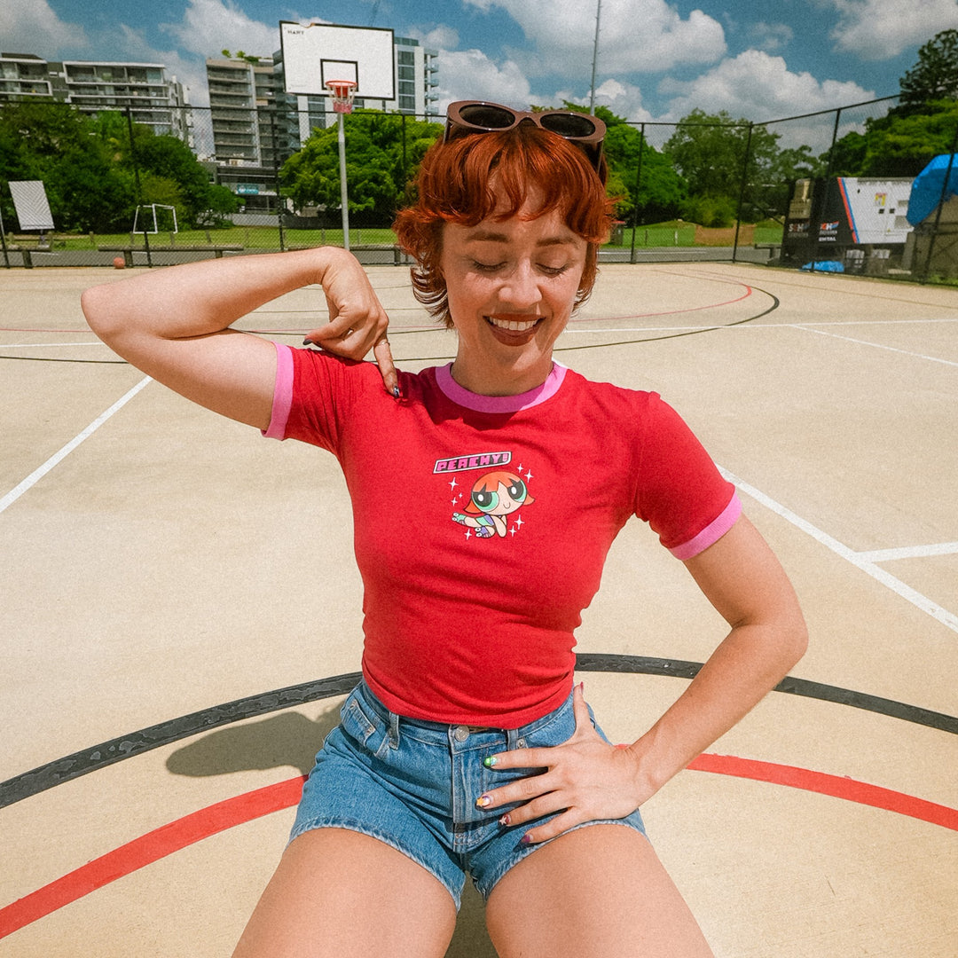 Peachy in her red signature baby tee and denim shorts posing on a basketball court
