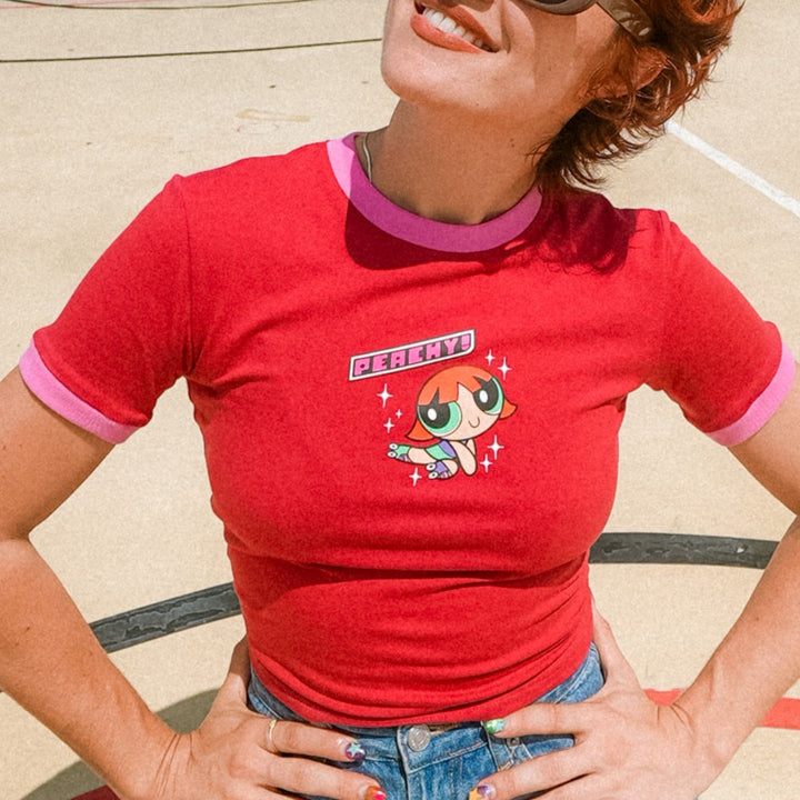 Peachy wearing a red baby tee with her personal cartoon character design outdoors.