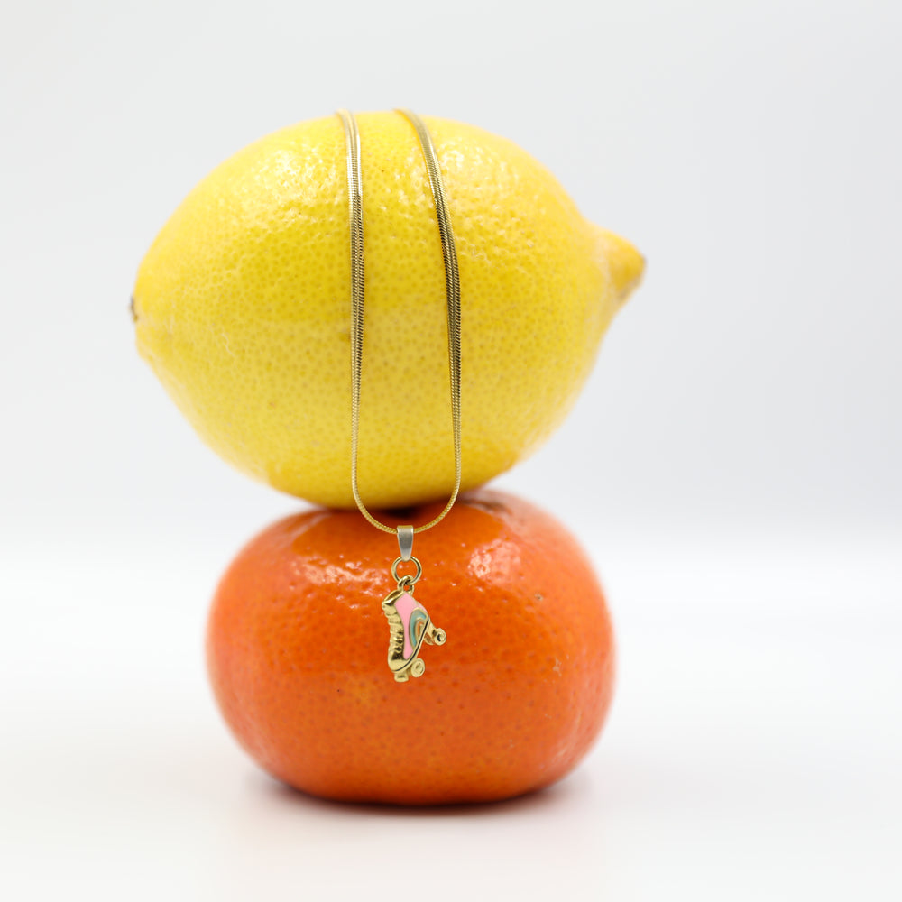 Gold necklace with rollerskate pendant charm draped over a lemon and orange on a white background