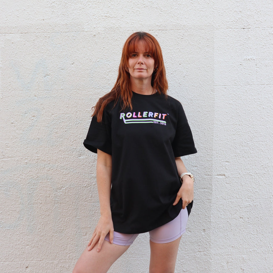 Person wearing a black 'ROLLERFIT' oversized t-shirt against a light gray wall
