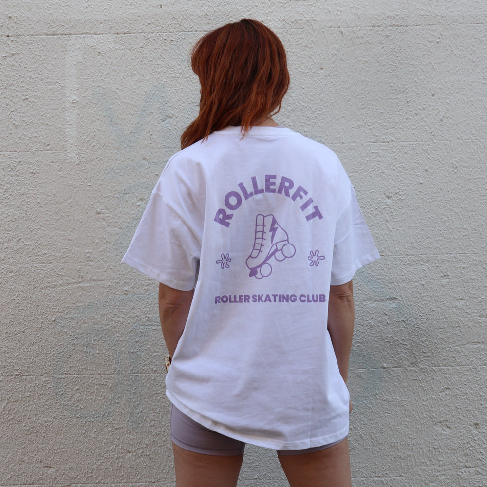 Person wearing a white t-shirt with purple 'ROLLERFIT' and 'ROLLER SKATING CLUB' text and graphics against a plain wall.