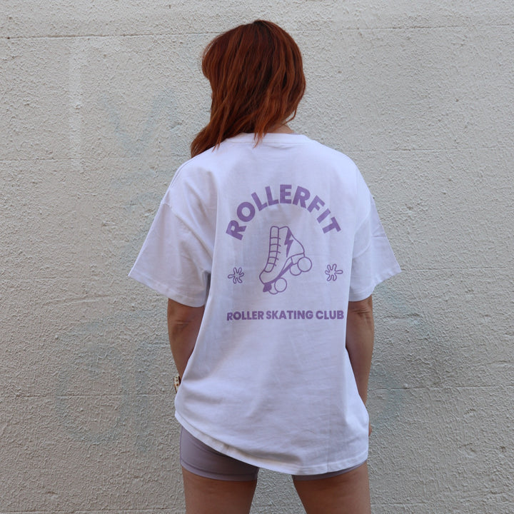 Person wearing a white t-shirt with purple 'ROLLERFIT' and 'ROLLER SKATING CLUB' text and graphics against a plain wall.