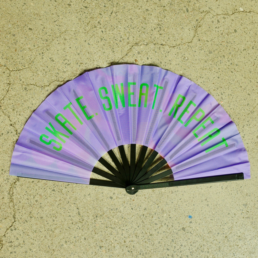 RollerFit handheld fan with black spine, purple design with green bold Skate. Sweat. Repeat text.