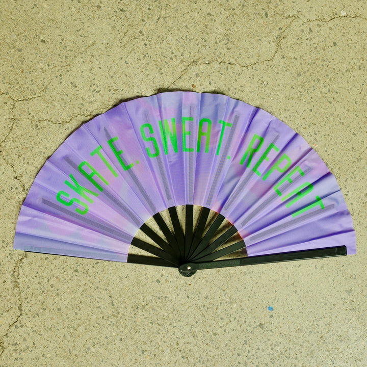 RollerFit handheld fan with black spine, purple design with green bold Skate. Sweat. Repeat text.