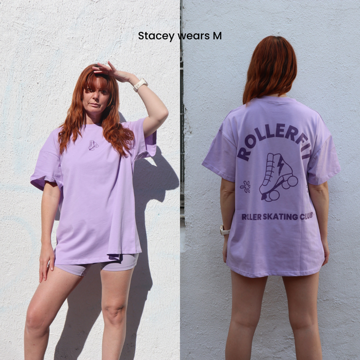 Woman wearing a lilac oversized t-shirt with RollerFit roller skating club branding, standing against a plain wall.