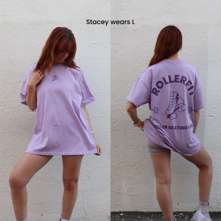 Woman wearing a lilac oversized t-shirt with RollerFit roller skating club branding, standing against a plain wall.