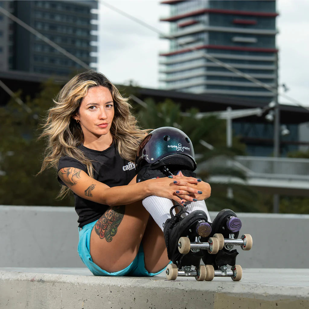 Barbie Patin sits on a concrete ledge knees towards her chest, wearing her pro roller skates and her pro Triple 8 Deep Cover helmet resting on her knees.