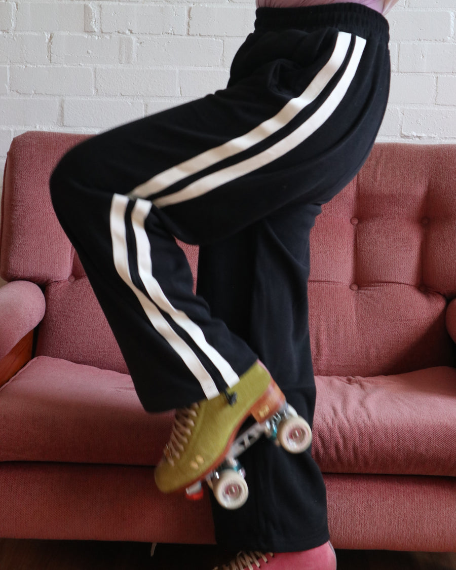 Stacey wears the black wide leg stripe track pants from the RollerFit Shop with her roller skates