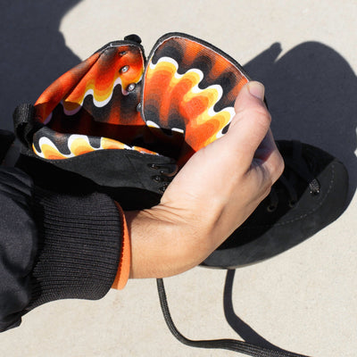 Sugu's hand holding open Chuffed Skates De La Casa Pro Boots, black roller skate boots with a retro black, orange, yellow and white gradient wave lining.