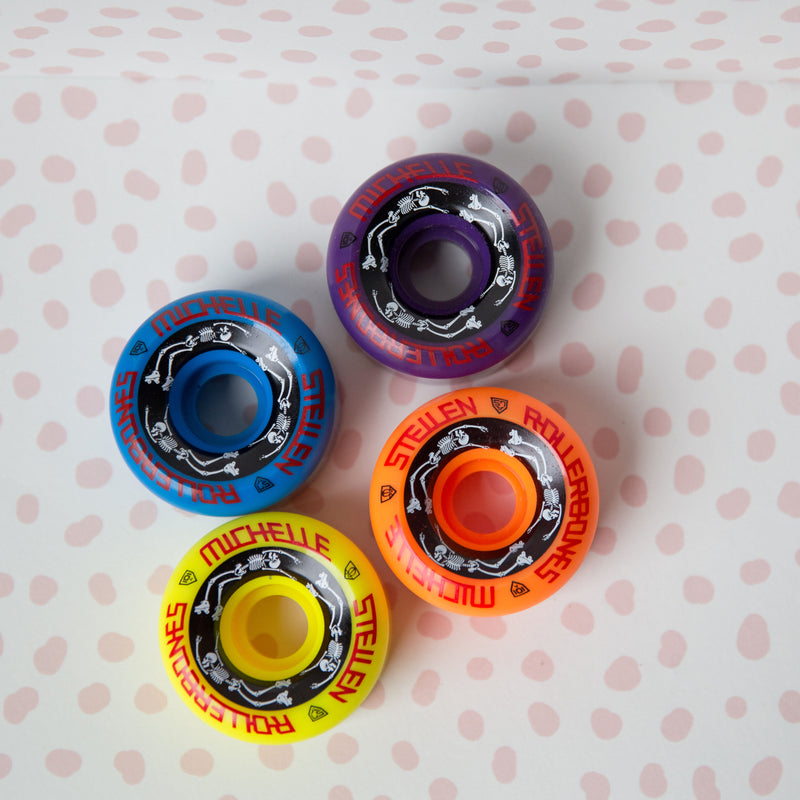 Rollerbones x Michelle Steilen Bowl Bomber wheels 4 pack with 1 purple, 1 orange, 1 yellow and 1 blue wheel with black, white and red print.