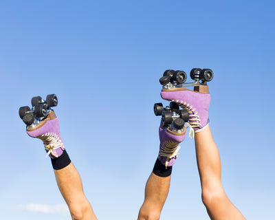 3 legs against a blue sky wearing Chuffed Skates Wanderer roller skates in Jacaranda Purple.