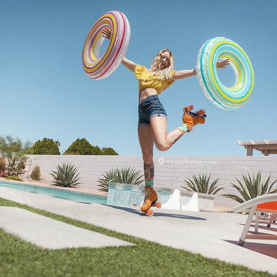 Karli stands by a pool on one toe stop of Clementine Lolly roller skates with arms up holding pool tubes.