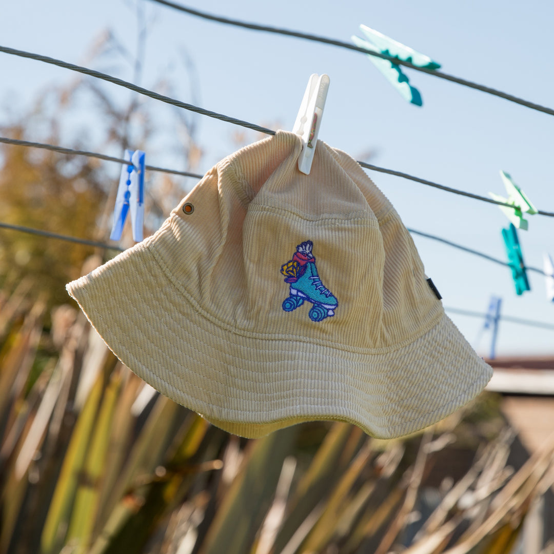 RollerFit Sand Galah bucket hat, sandy cream colour with blue roller skate and pink galah embroidered design.
