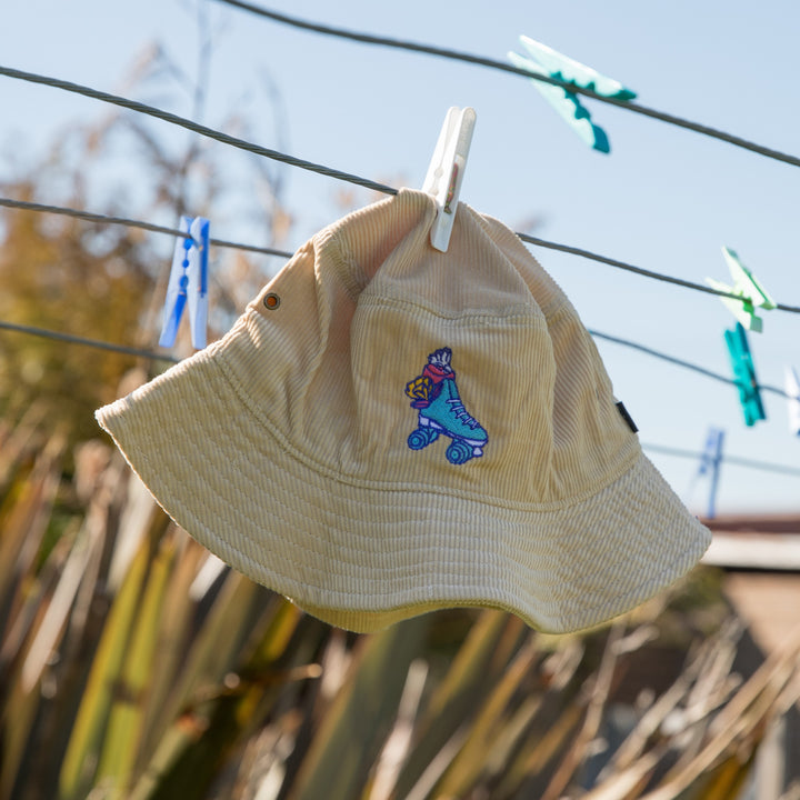 RollerFit Sand Galah bucket hat, sandy cream colour with blue roller skate and pink galah embroidered design.