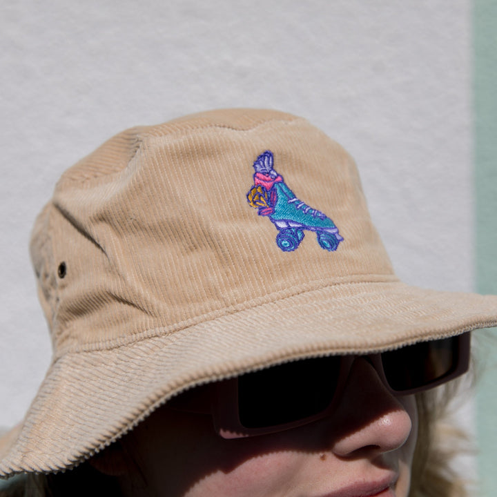 RollerFit Sand Galah bucket hat, sandy cream colour with blue roller skate and pink galah embroidered design.