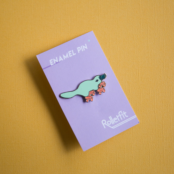 RollerFit enamel pin platypus in aqua with orange glitter skates and glitter dark teal beak.